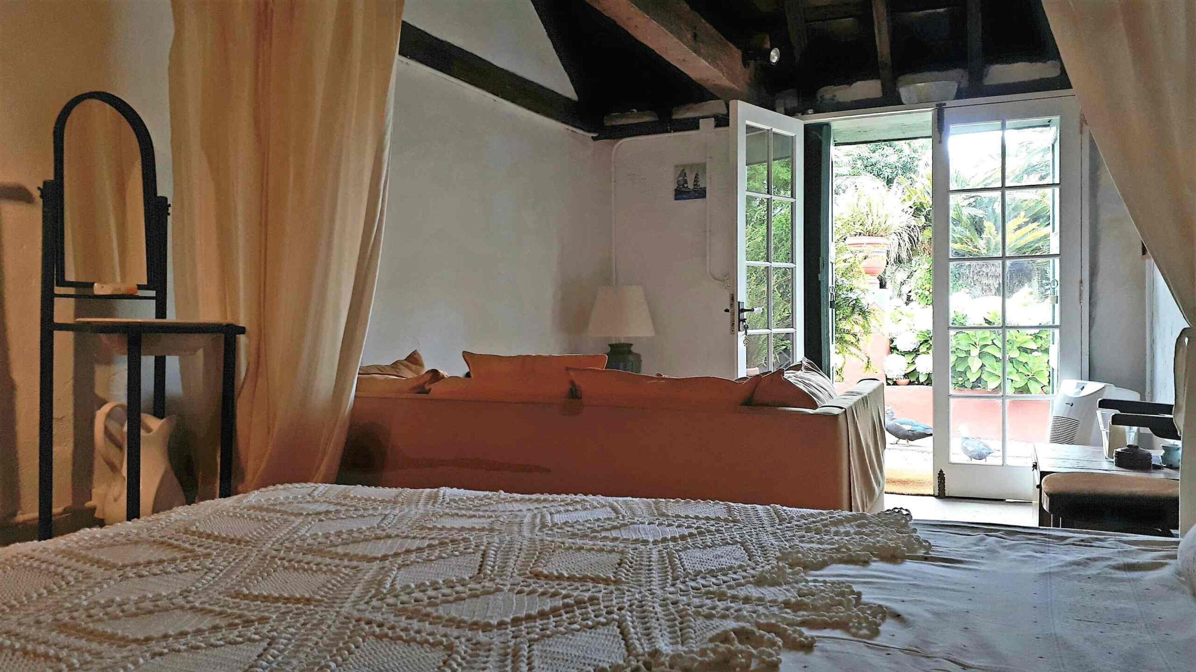 A bedroom with a bed, a nightstand, a lamp, and a window with a view of greenery.