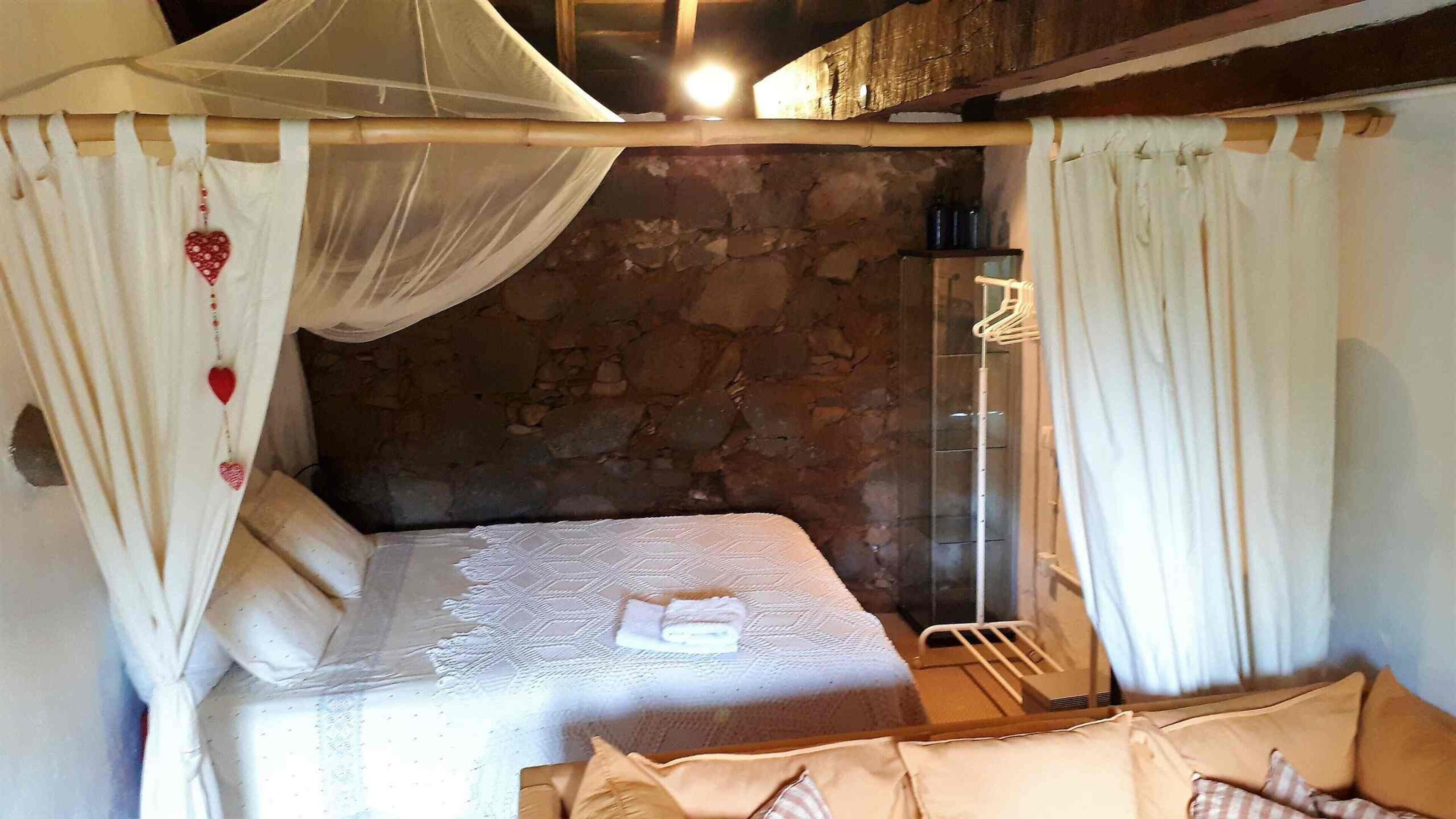 Un dormitorio con pared de piedra, cama con dosel y perchero.