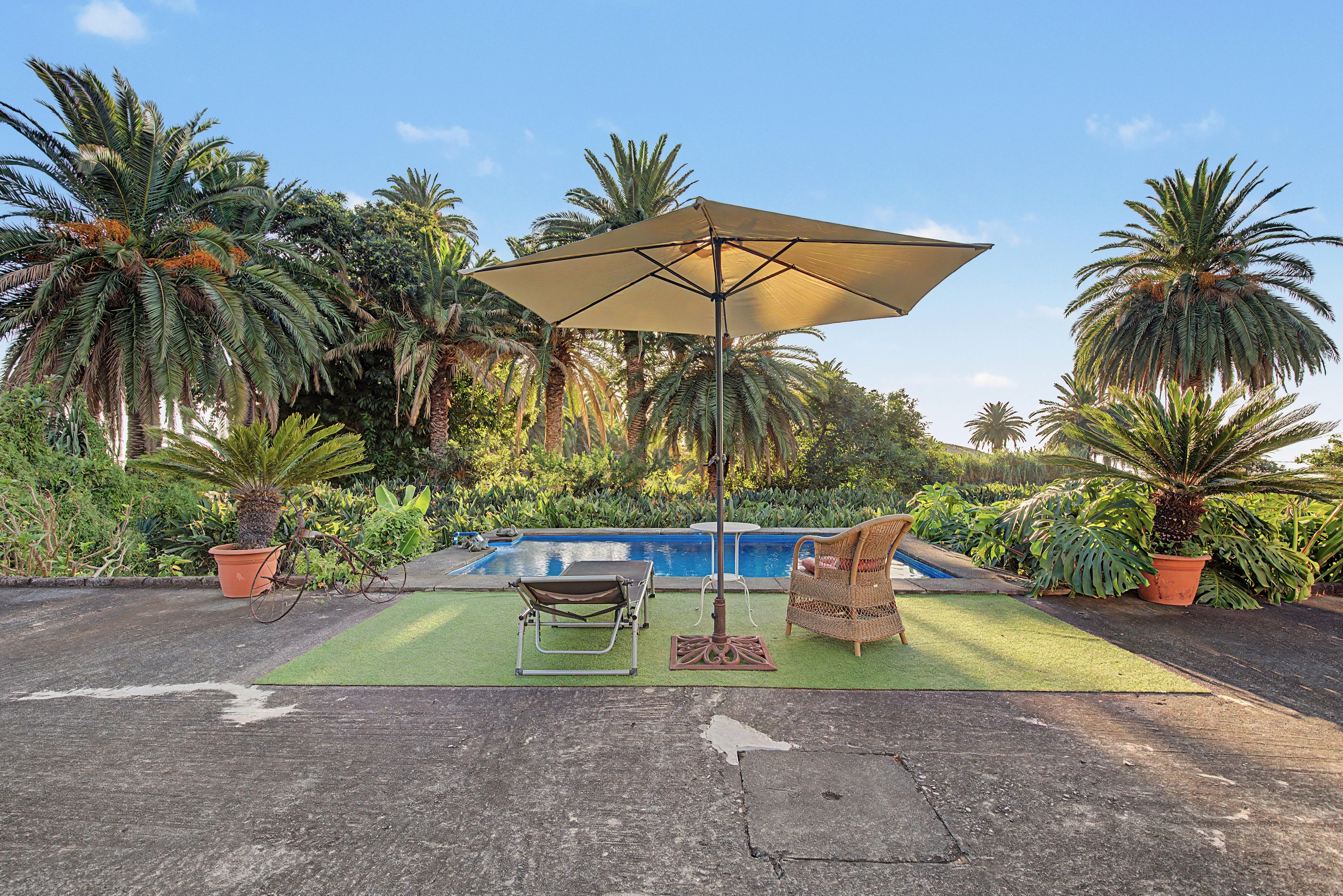 Un área junto a la piscina con una silla de descanso, una mesita y una sombrilla.
