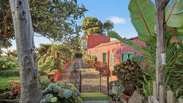 Un sendero conduce a un edificio con fachada roja, rodeado de exuberante vegetación y plantas tropicales.