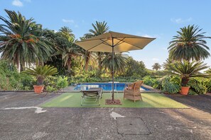 Un área junto a la piscina con una silla de descanso, una mesita y una sombrilla.