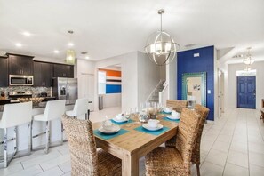 Une cuisine moderne avec des meubles de couleur sombre, des appareils en acier inoxydable et un coin repas comprenant une table en bois et des chaises en osier.