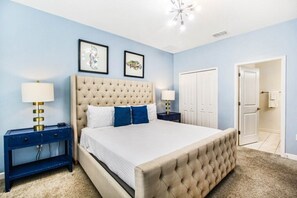 Une chambre à coucher avec un grand lit, deux tables de chevet, un luminaire au plafond et deux tableaux encadrés accrochés au mur.