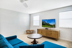 A living room with a blue sofa, a round table, a wooden cabinet, and a mounted TV. - 6BR Modern Disney area -ChampionsGate Pool/Spa Villa- Game Room (Davenport)
