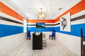 Une pièce dont un des murs est décoré de motifs rayés, ornée d’un lustre, comprenant une table avec des chaises et des œuvres d’art accrochées aux murs.