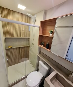 Ein modernes Badezimmer mit Duschkabine aus Glas, Toilette und Holzregal mit einer kleinen Pflanze.