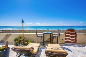 Eine Terrasse mit Blick auf den Ozean, ausgestattet mit einem Tisch, Stühlen und einer Lounge-Ecke.