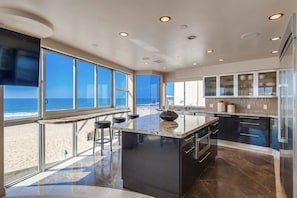 A modern kitchen with a large island, bar stools, and a view of the beach. - Boardwalk Paradise 2 | New Mid-Stay Home w/ Endless Sunsets (San Diego)