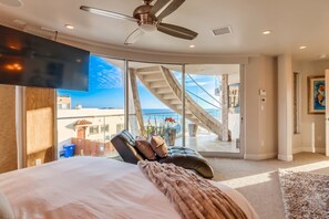 A bedroom with a large bed, a chair, a television, and a view of the beach and staircase. - Boardwalk Paradise 2 | New Mid-Stay Home w/ Endless Sunsets (San Diego)