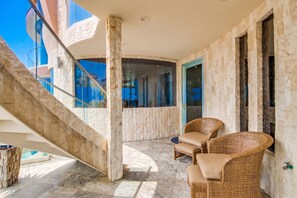 A balcony with a stone wall, a glass door, and wicker furniture. - Boardwalk Paradise 2 | New Mid-Stay Home w/ Endless Sunsets (San Diego)