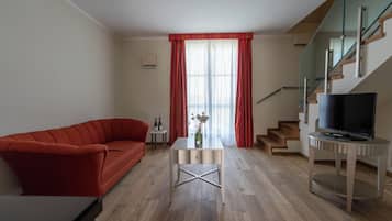 Un salon moderne avec un canapé rouge, une petite table sur laquelle est posé un vase, un téléviseur sur un meuble et un escalier doté de rampes en verre.