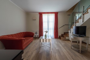 Ett modernt vardagsrum med en röd soffa, ett litet bord med en vas, en tv på ett tv-bord och en trappa med glasräcken.