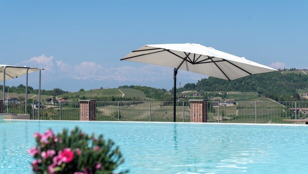 A swimming pool with a view of a hilly landscape and a fence. - LOSTU Monforte (Monforte d'Alba)