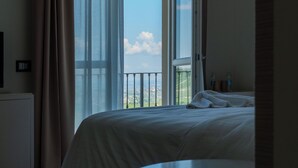 A hotel room with a bed, a round table, and a large window with curtains. - LOSTU Monforte (Monforte d'Alba)