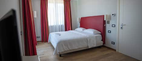 A hotel room with a bed, a TV, and a door.