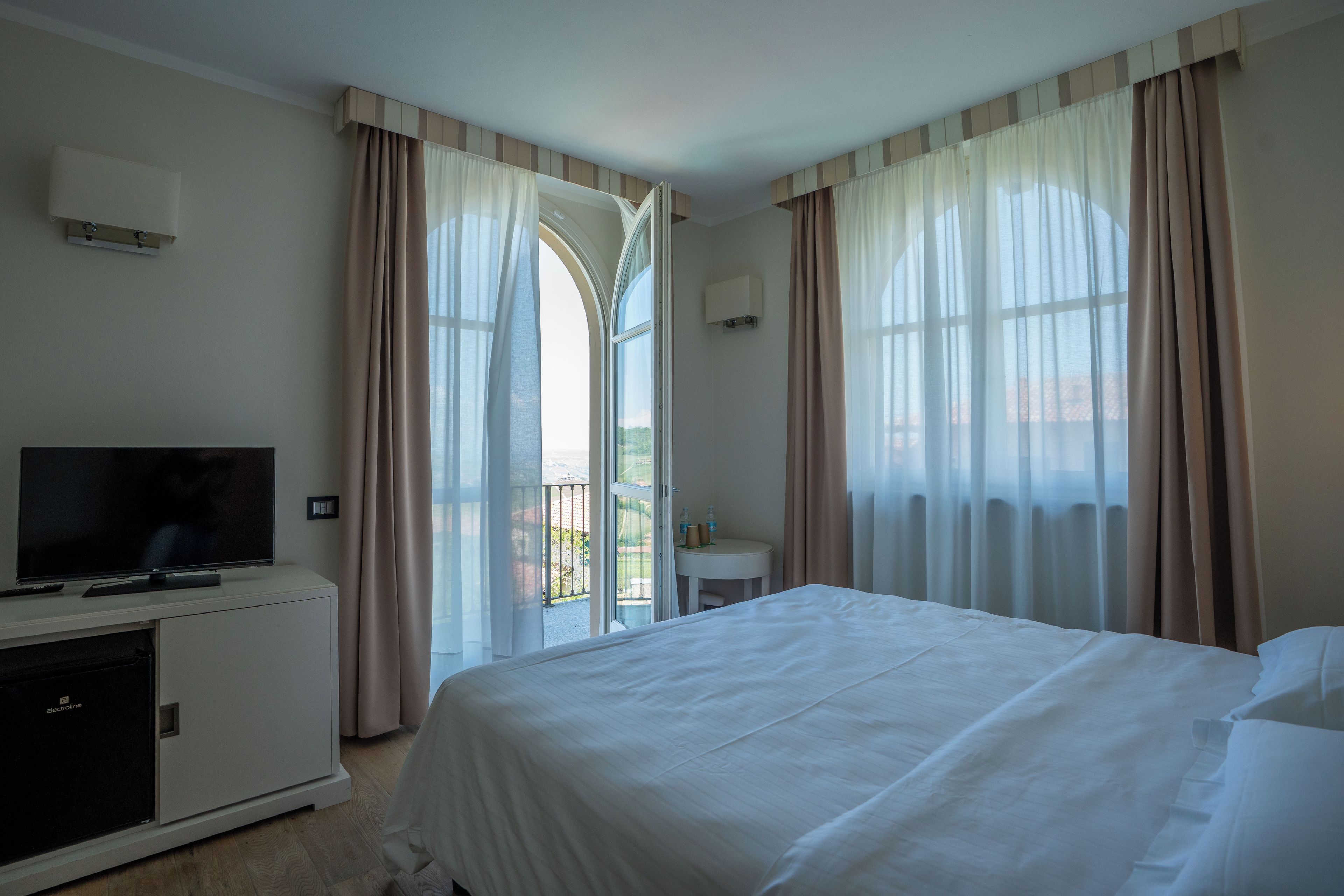 Una camera d'albergo con un letto, una televisione, una scrivania e vista sull'esterno tramite ampie finestre.