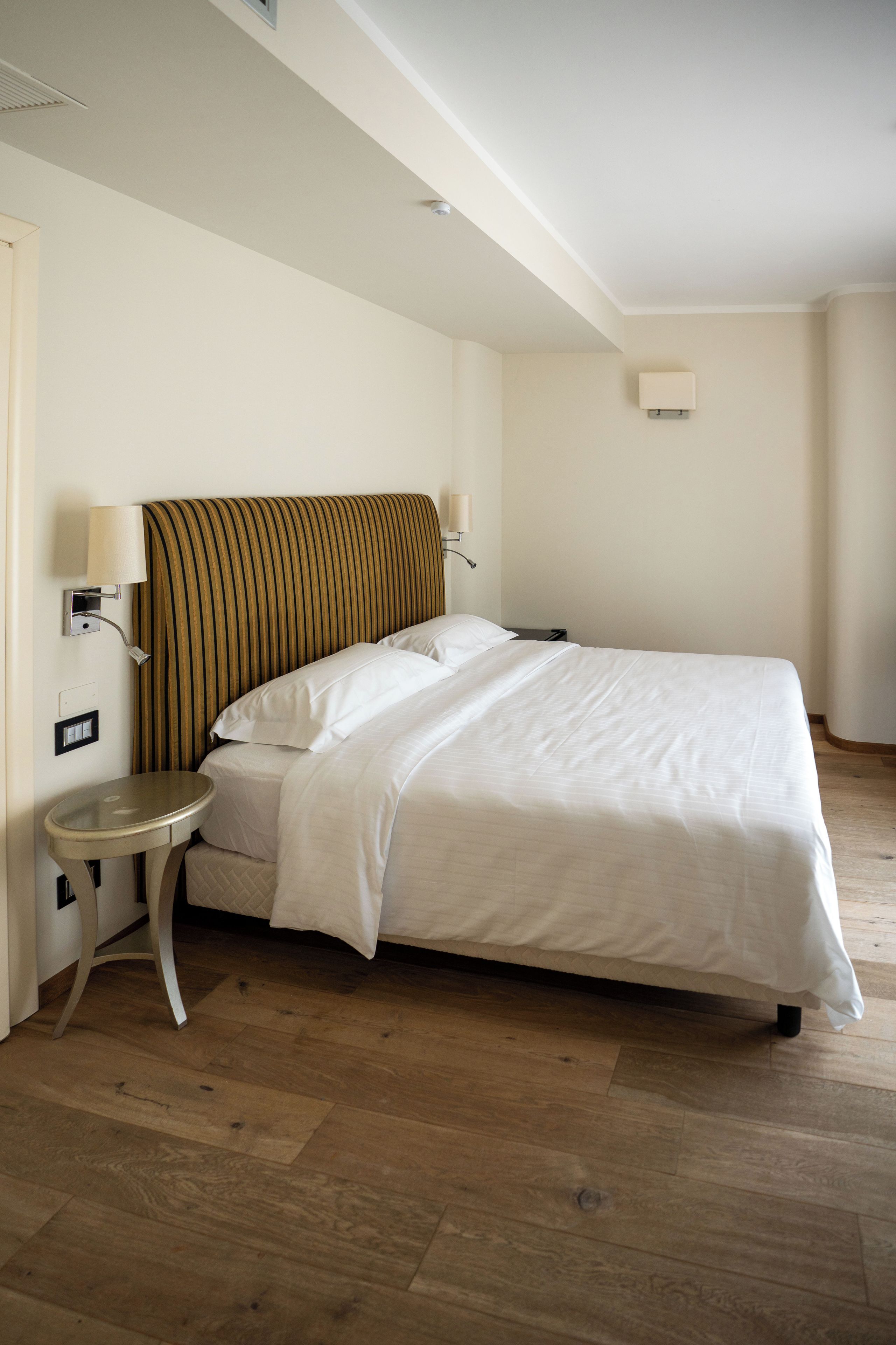 A hotel room with a single bed, a bedside table, a lamp, and a wall-mounted light.