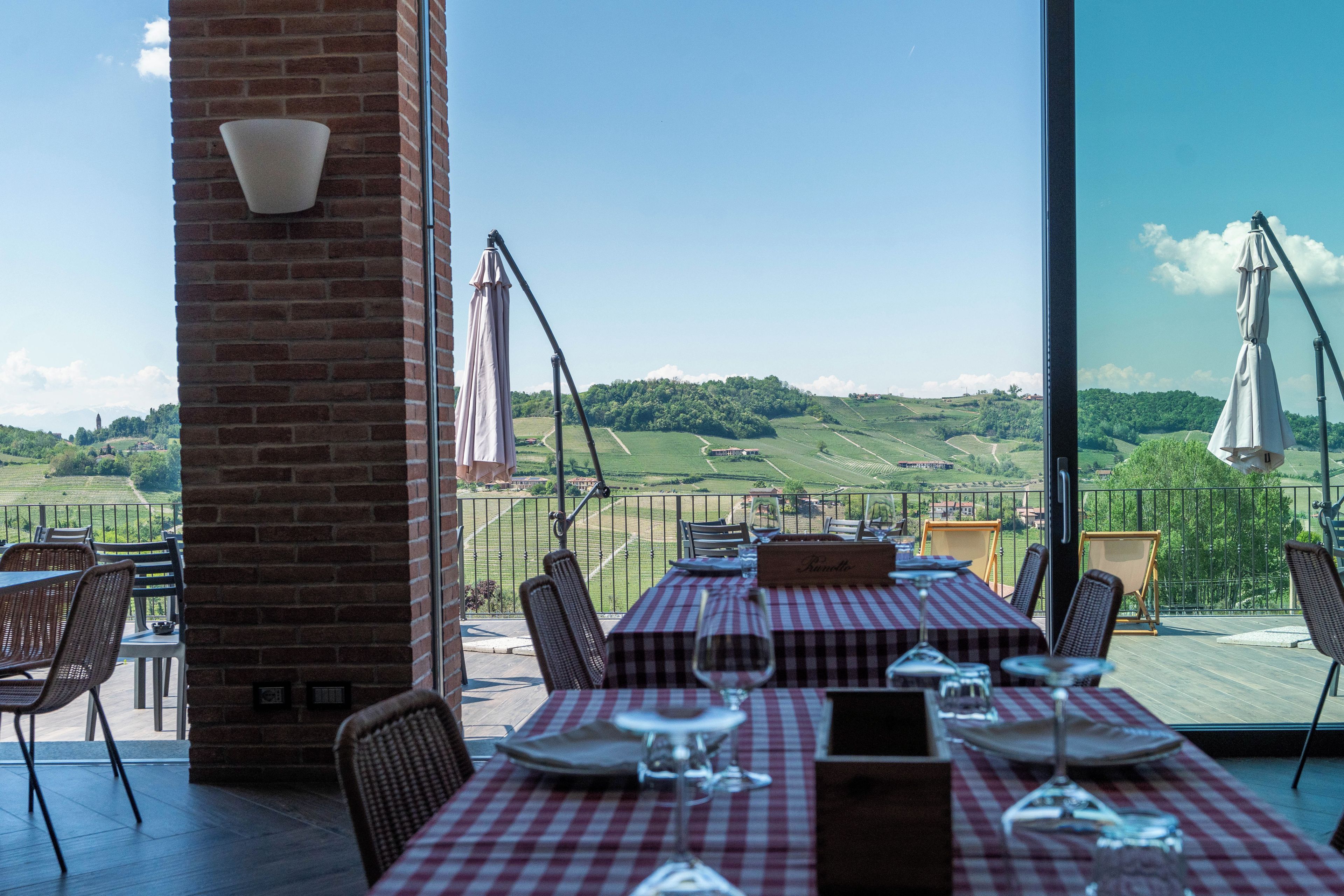 Un espace de restauration en plein air offrant une vue sur des collines verdoyantes, agrémenté d’une colonne en briques et d’une nappe à carreaux.