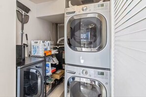 Een wasserette met gestapelde wasmachines, een droogrek en planken met schoonmaakmiddelen.