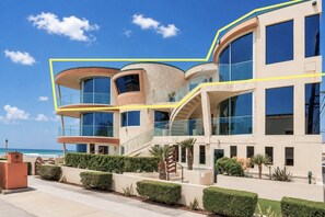 Un edificio de varios pisos con balcones, ventanas grandes y vista al mar.
