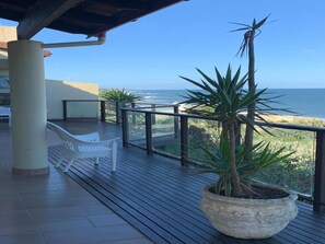 A wooden deck with a potted plant, a white bench, and a view of the ocean.