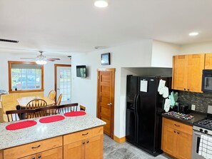 A kitchen with wooden cabinets, a black refrigerator, a stove, and a dining area with a table and chairs.