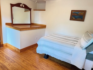 A bedroom with a wooden headboard, a bed with a striped bedspread, a wall-mounted mirror, and a painting.