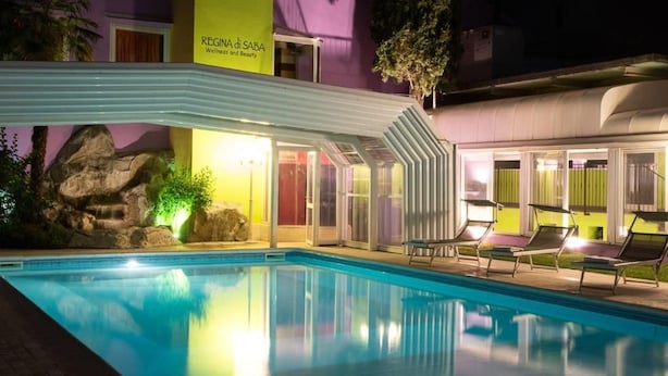 Une piscine avec des chaises longues, une formation rocheuse et un bâtiment sur lequel est apposée une enseigne indiquant : « REGINA di SABA, centre de bien-être et de beauté ».