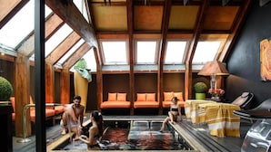 Un espace détente avec un jacuzzi, des poutres en bois, des sièges orange et une vue dégagée grâce à de grandes fenêtres.