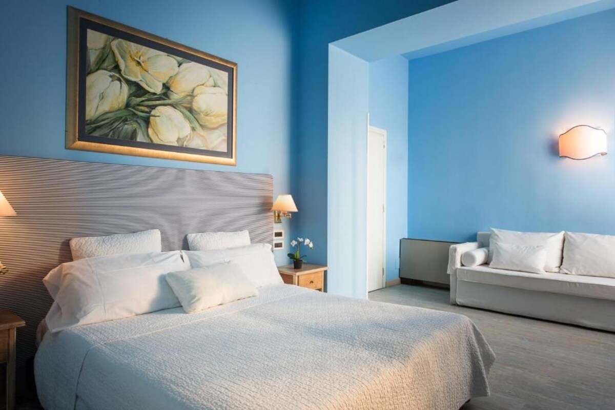 Une chambre d’hôtel comprenant un lit, une table de chevet avec une lampe, un canapé et un luminaire fixé au mur.