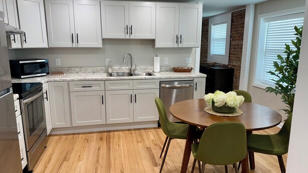 A modern kitchen with white cabinets, a stainless steel sink, and a dining area with a wooden table and green chairs.