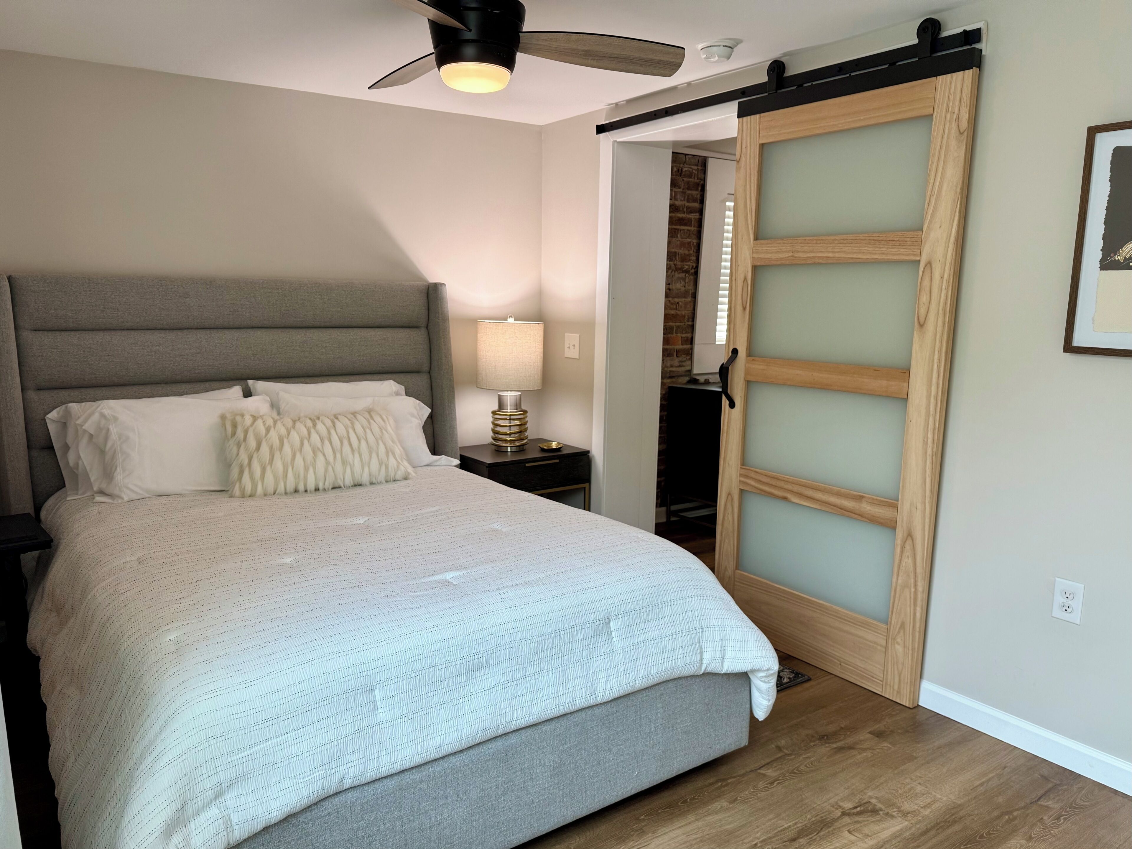 A bedroom with a bed, a nightstand, a lamp, a ceiling fan, and a sliding door.