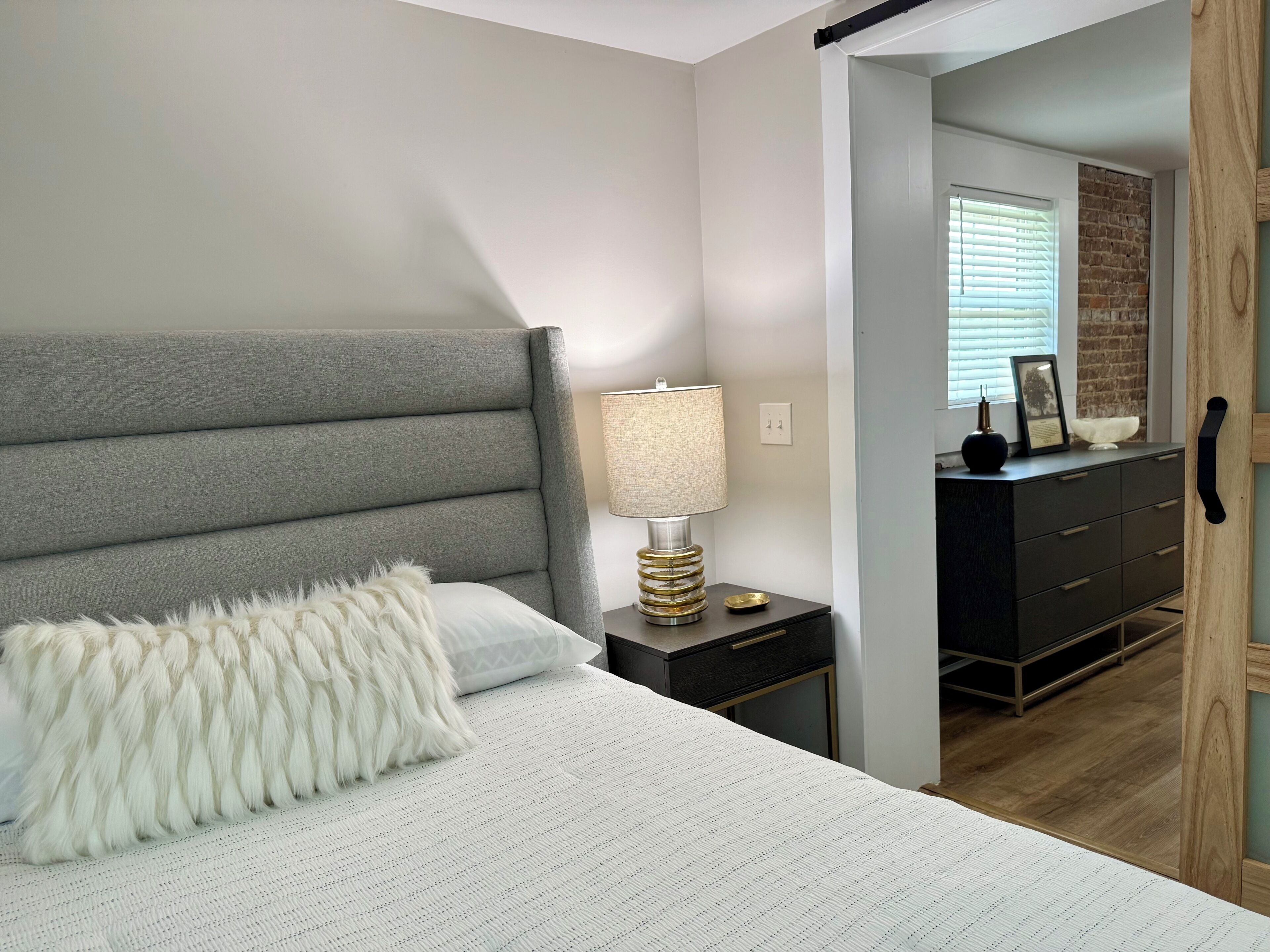 A bedroom with a bed, a nightstand, a lamp, a dresser, and a door.
