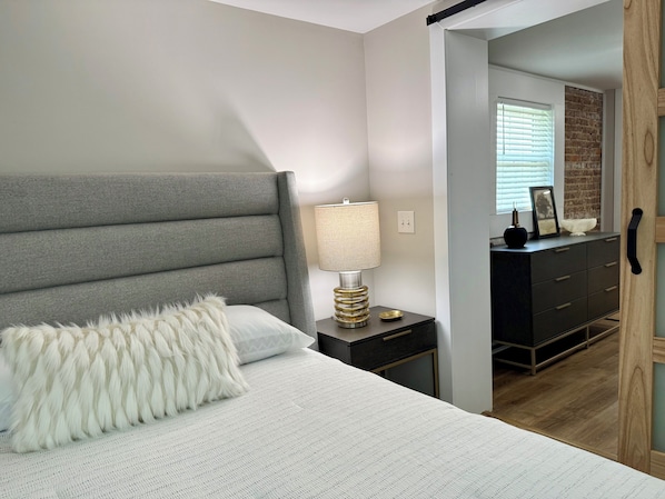A bedroom with a bed, a nightstand, a lamp, a dresser, and a door.