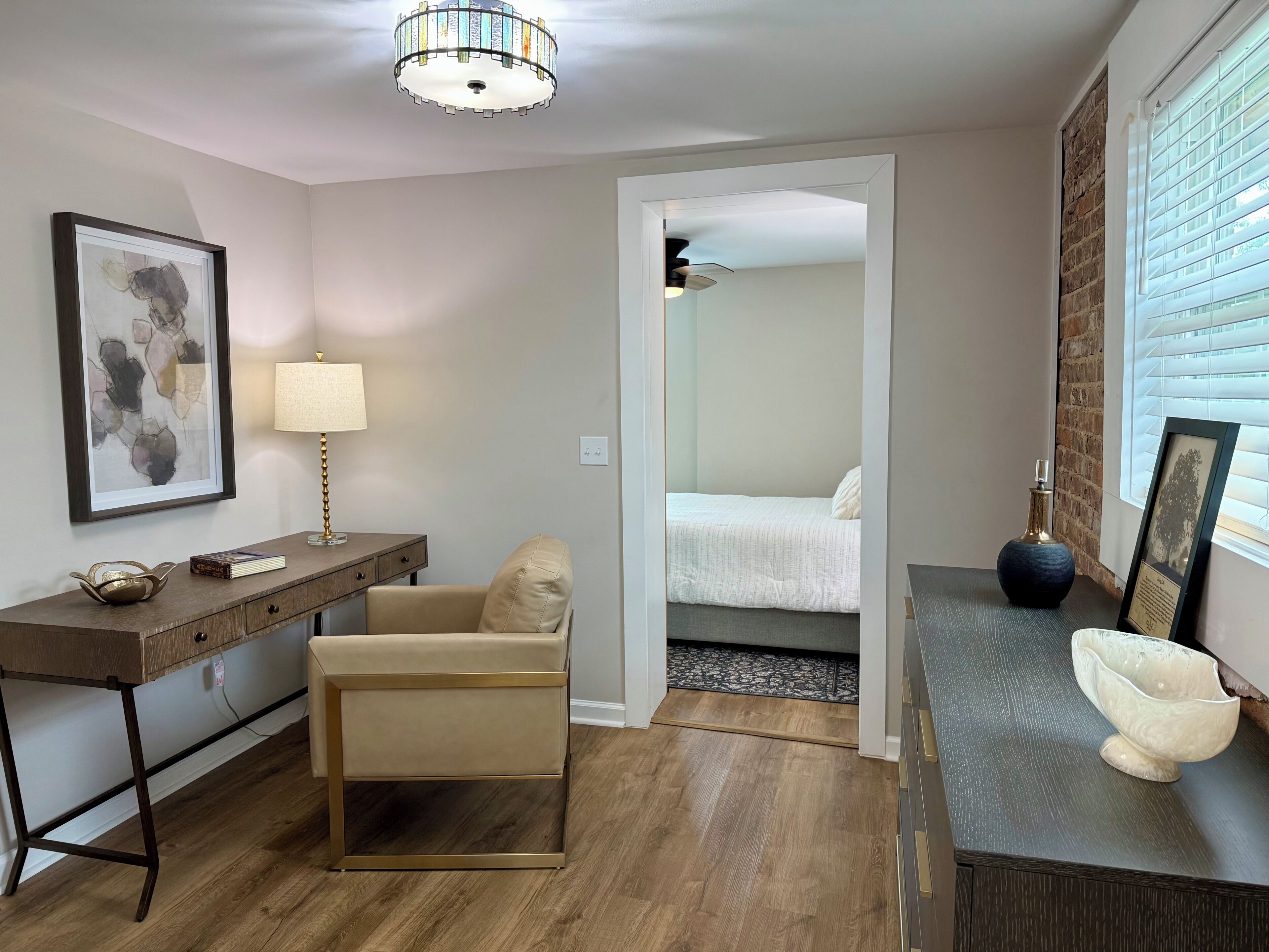 A modern room with a desk, chair, bedside table, lamp, and a bed.