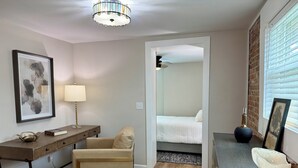 Una habitación moderna con escritorio, silla, mesita de noche, lámpara y una cama.