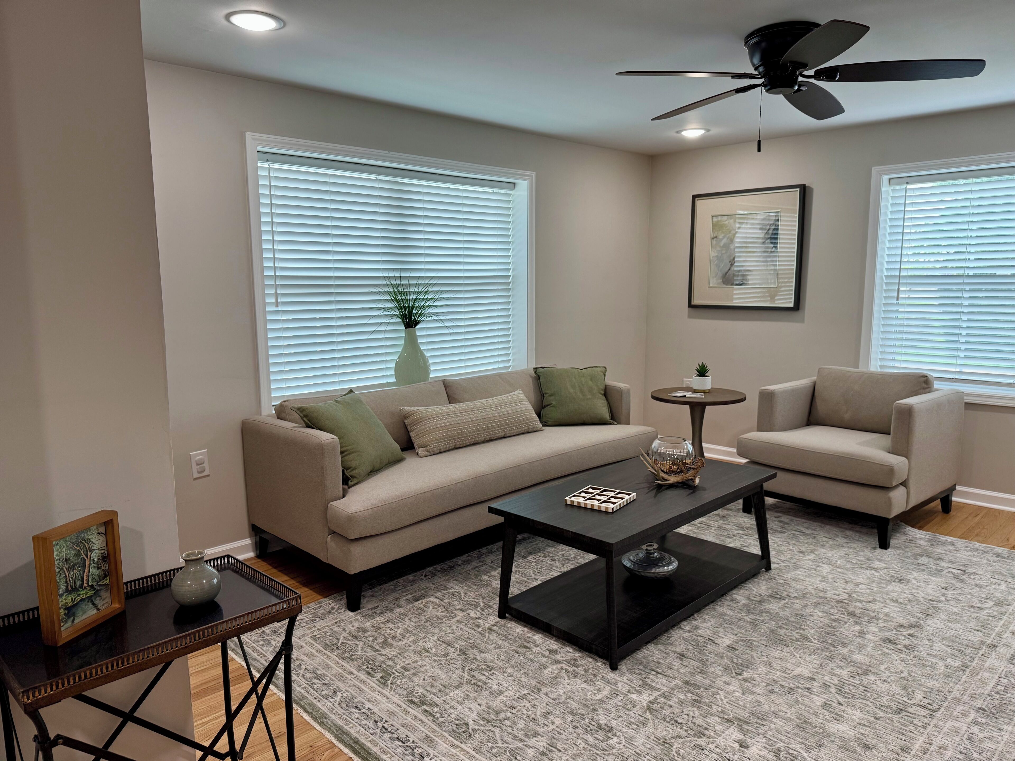 A living room with a sofa, armchairs, a coffee table, and a ceiling fan.