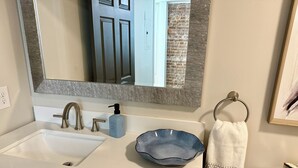 Un baño con un lavamanos blanco, un dispensador de jabón azul, un tozalete y un inodoro.