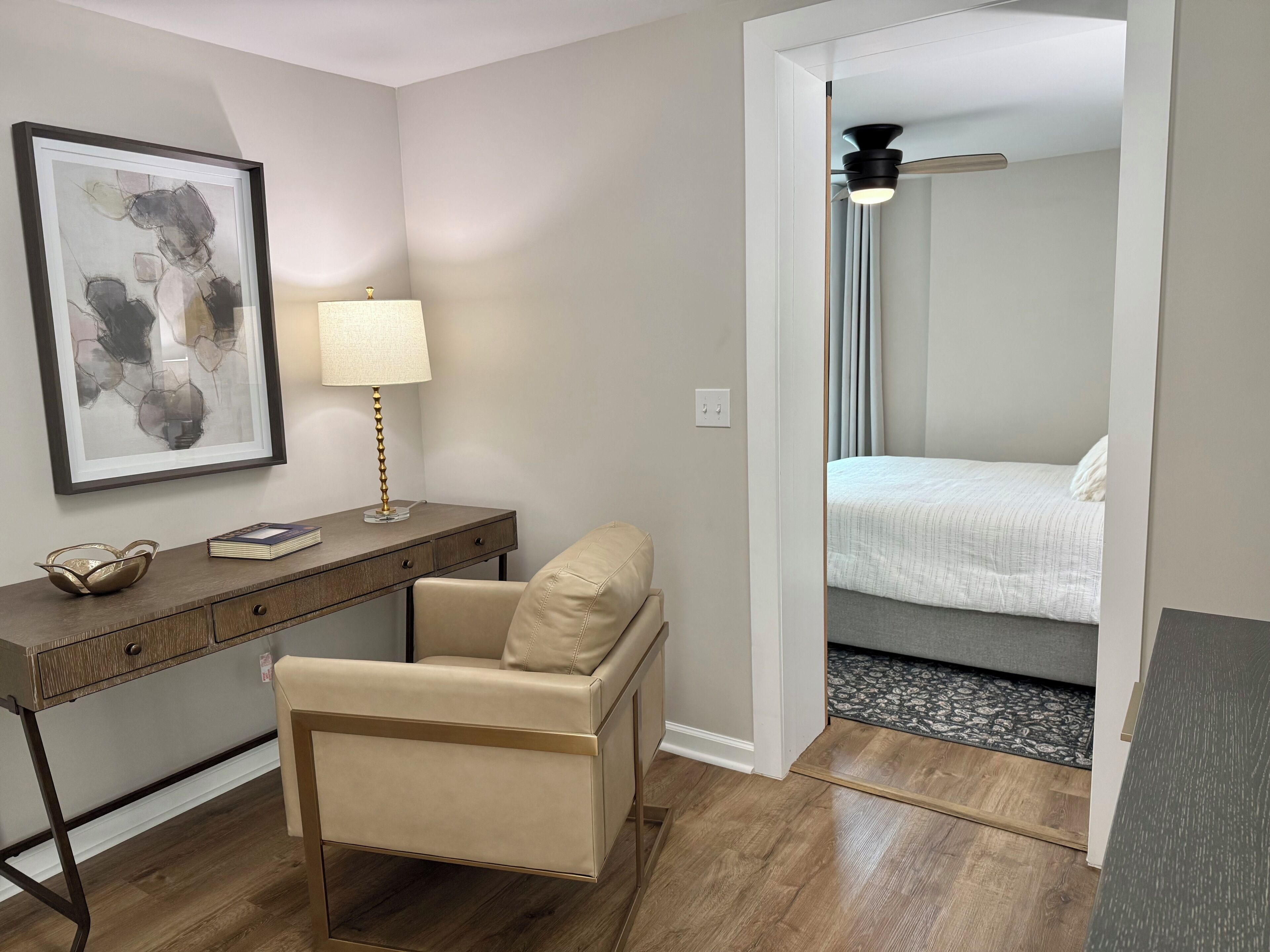 A hotel room with a desk, chair, bed, and a framed abstract painting.