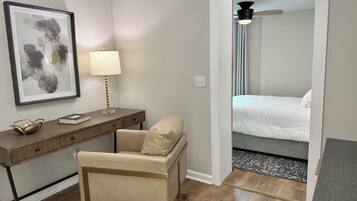 A hotel room with a desk, chair, bed, and a framed abstract painting.