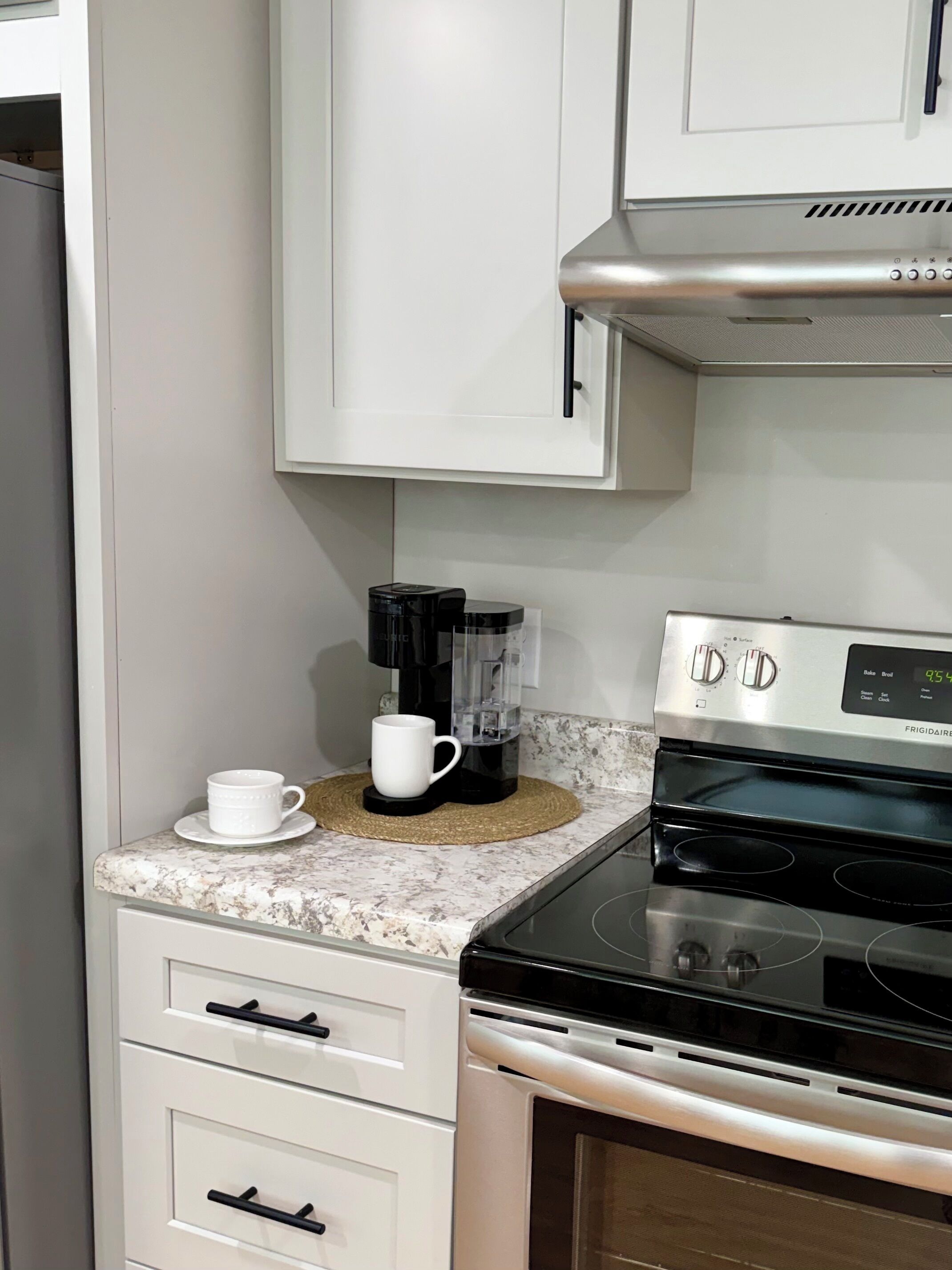A kitchen with white cabinets, a black stove, and a coffee maker on the countertop.