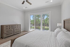 A bedroom with a large bed, a wooden dresser, and a view of a garden through a sliding glass door. - 30A House Co: The Henderson House (SANTA RSA BCH)