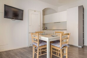 A dining area with a white table, four wooden chairs, and a television mounted on the wall. - Appartamento Dogana by Wonderful Italy (Peschiera del Garda)
