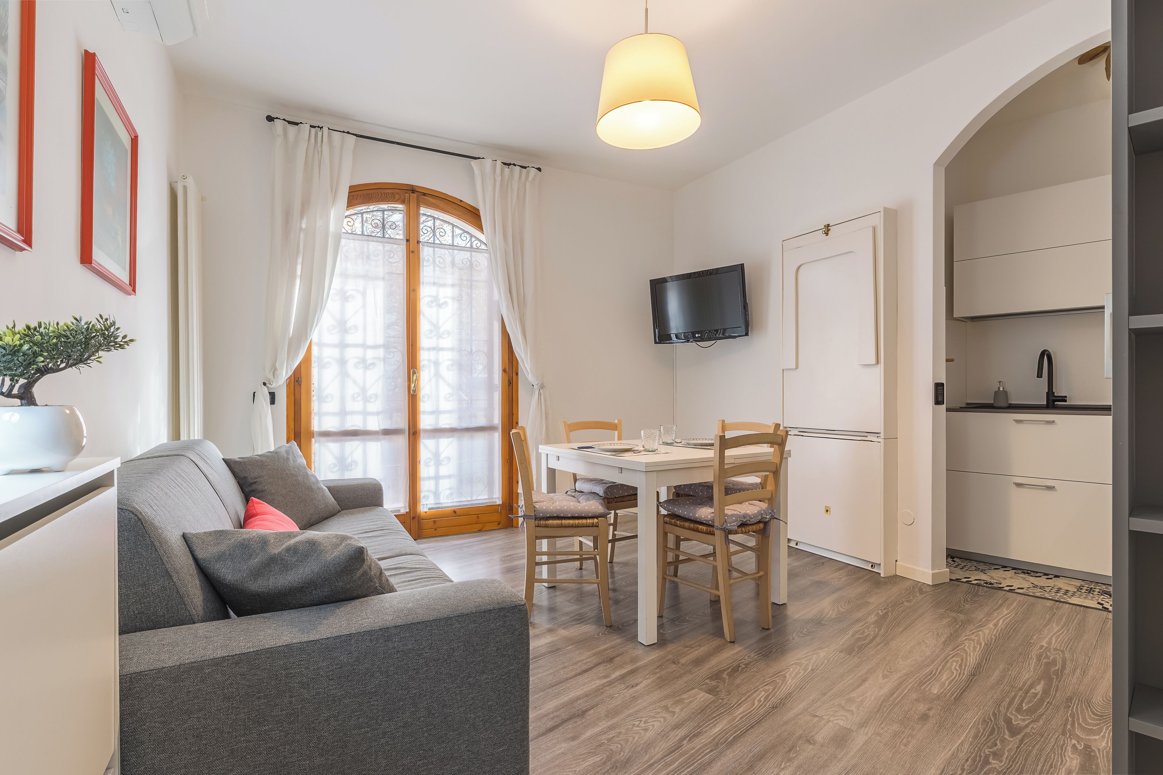 Un salon moderne avec un canapé, une table à manger et des chaises. Un téléviseur est fixé au mur et il y a un coin cuisine avec des placards.