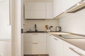 Uma cozinha moderna com armários brancos, uma torneira preta e uma chaleira no balcão.