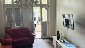 Una sala de estar con un sofá rojo, una mesa de centro blanca y un televisor sobre un mueble blanco.