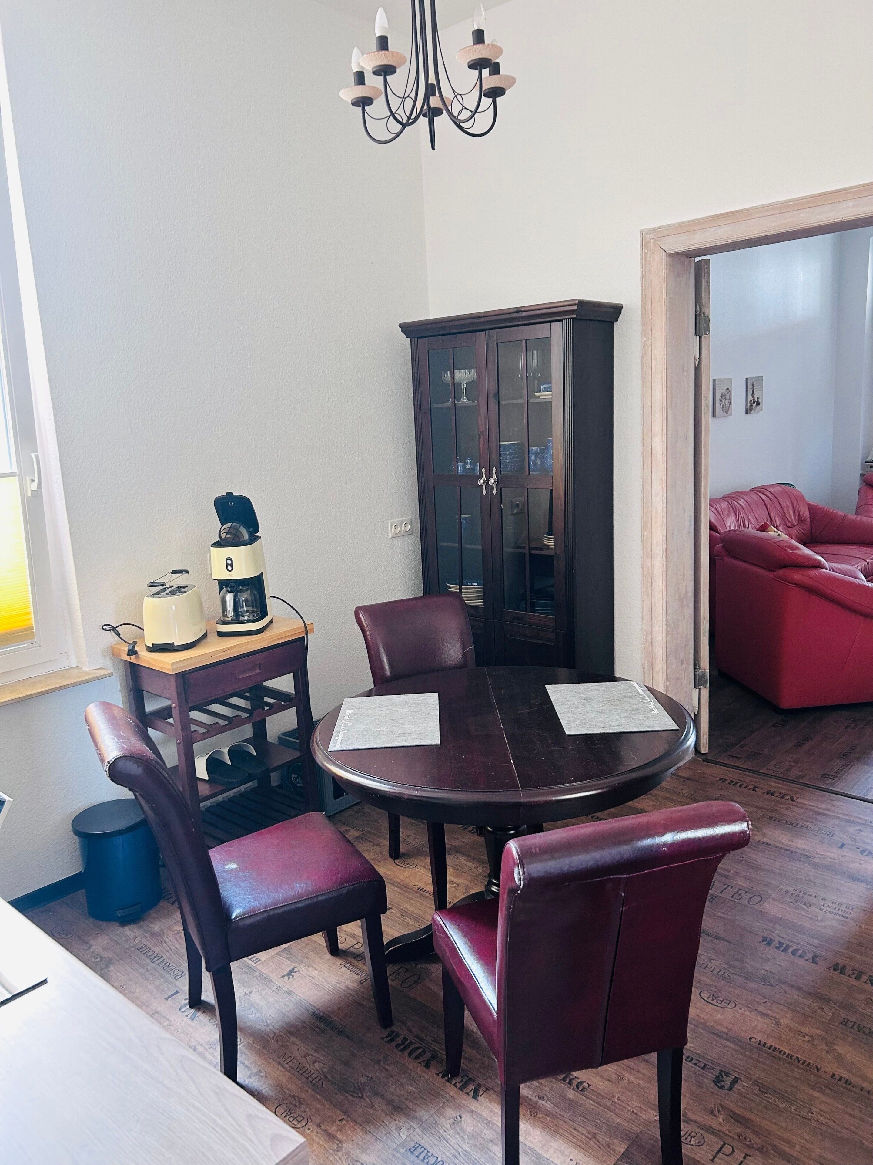 Un comedor con una mesa redonda, cuatro sillas, un aparador y un sofá rojo.