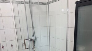 Cabina de ducha con paredes de vidrio, cabezal de ducha de mano y llave de pared.