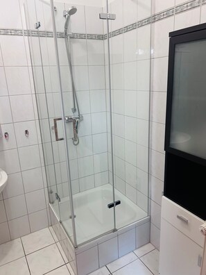 Cabina de ducha con paredes de vidrio, cabezal de ducha de mano y llave de pared.