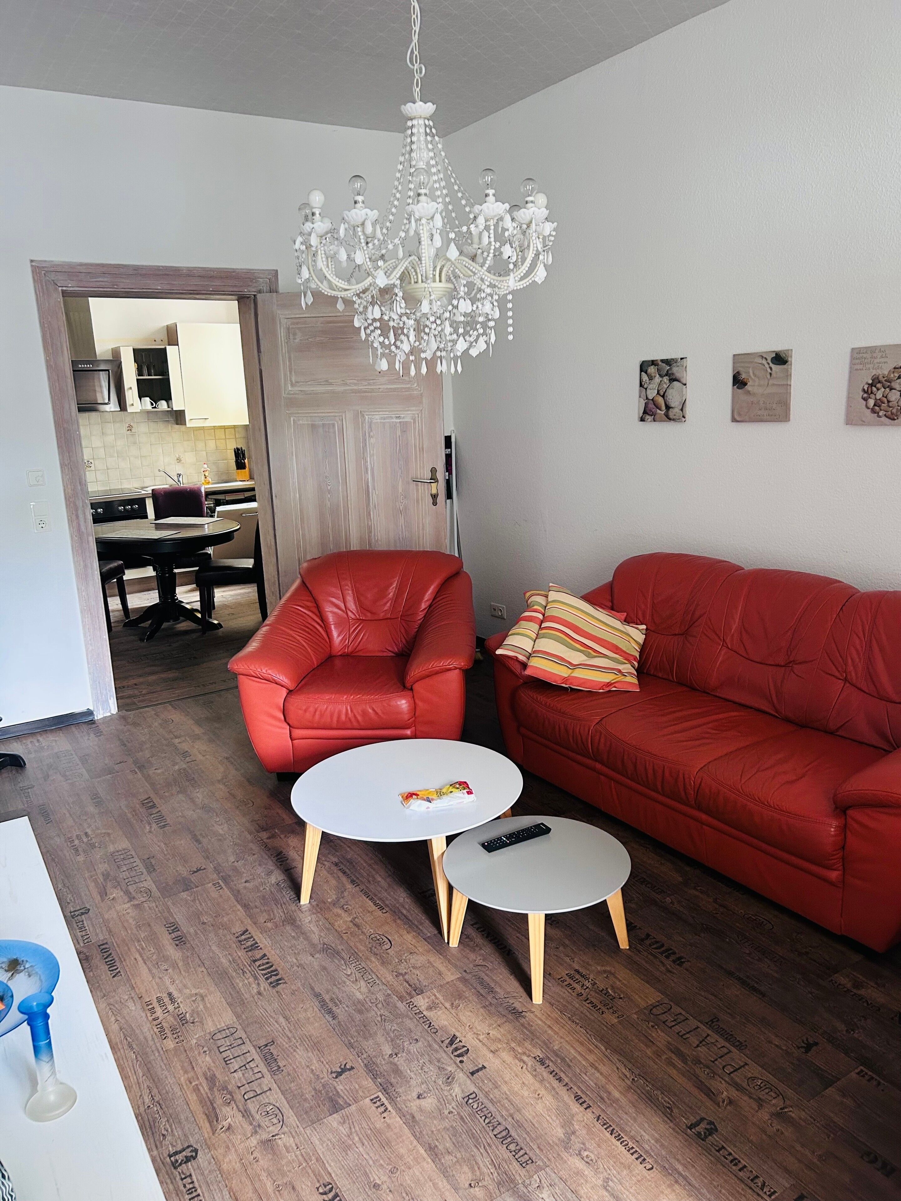 Una sala de estar con un sofá rojo, un sillón rojo, una mesa de centro blanca y una mesa redonda blanca. Hay una araña colgando del techo.